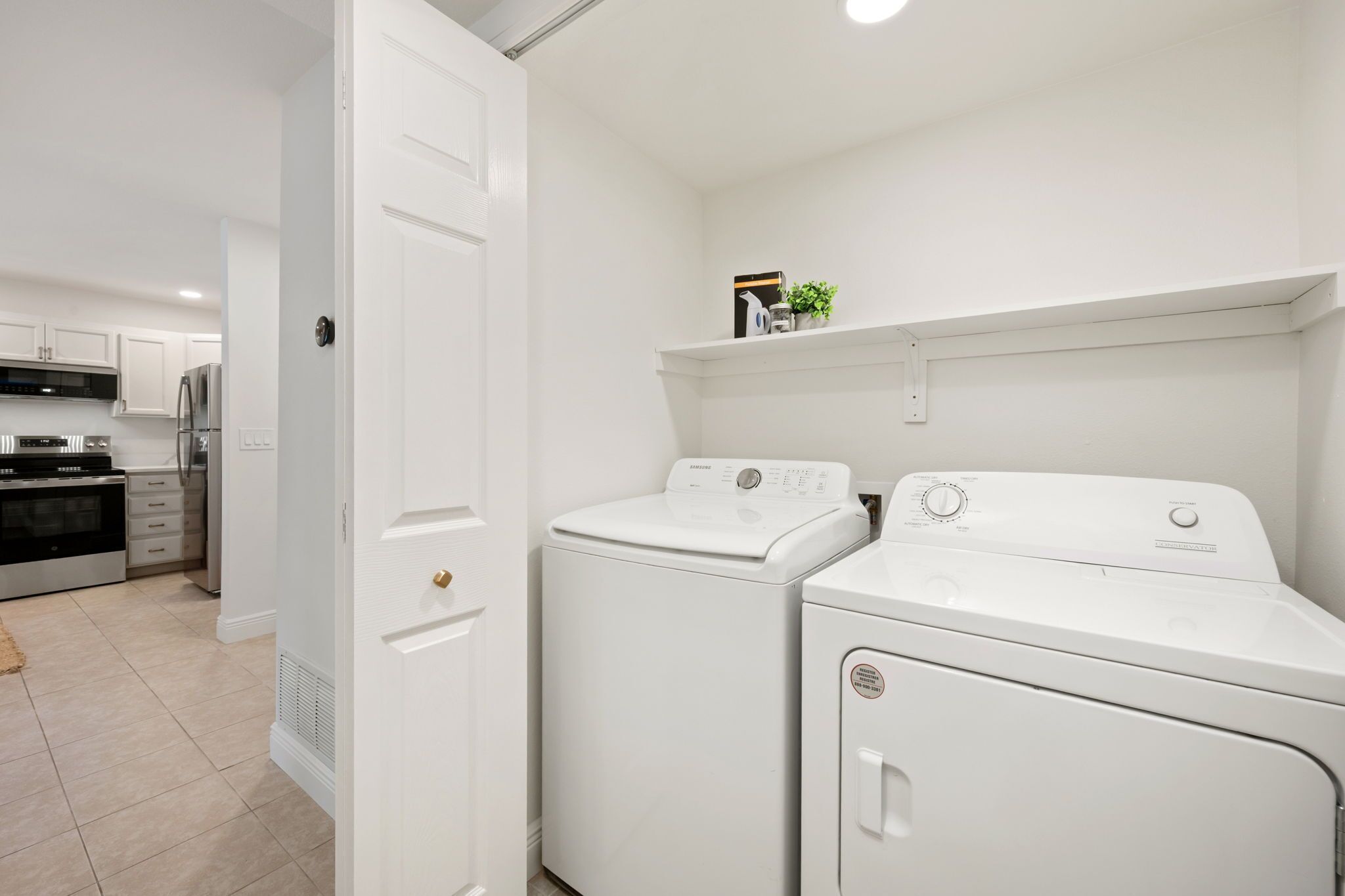 A laundry room with two front-loading washers and dryers, a white door, and a shelf above the dryers.