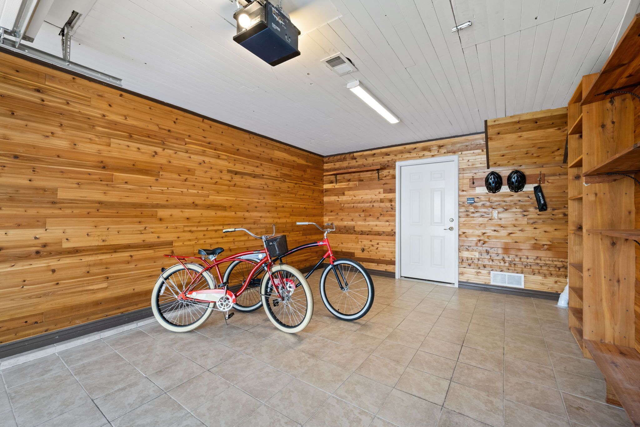 Une pièce aux murs en bois, avec un vélo, une porte et une étagère où sont rangés des casques.