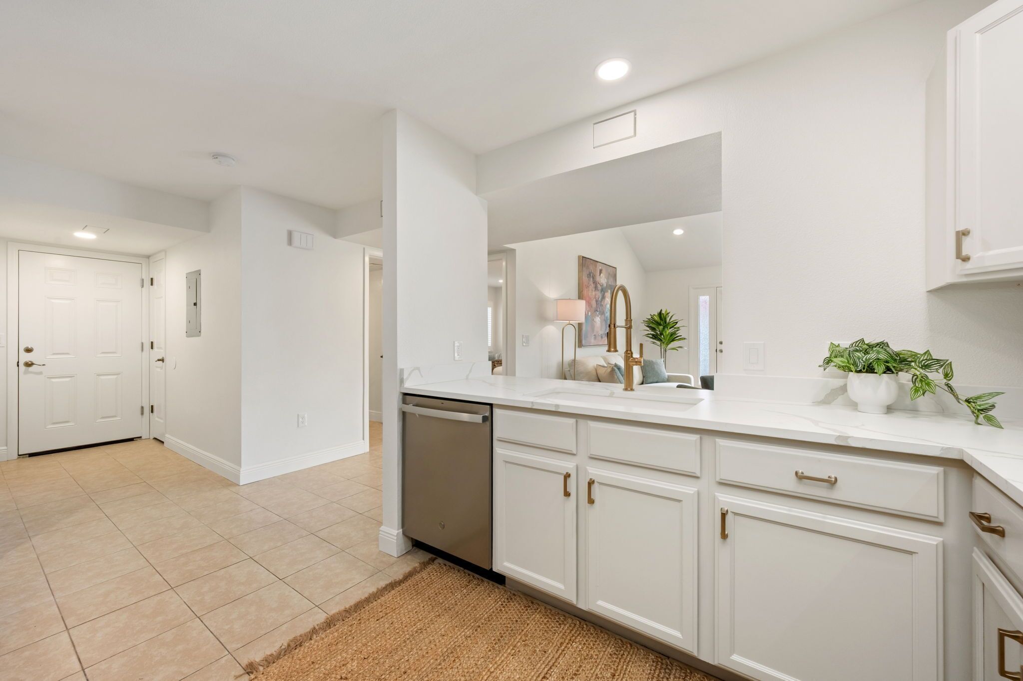 A modern kitchen with white cabinetry, a dishwasher, and a countertop with a sink and plants.