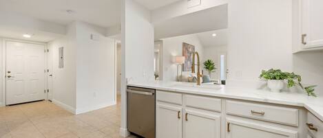 A modern kitchen with white cabinetry, a dishwasher, and a countertop with a sink and plants.