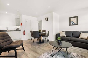 A modern living room with a sofa, a coffee table, and a dining area with chairs and a table. - Modern 1 Bedroom Apartment in Leeds - Sleeps 3 (Leeds)