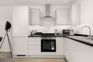 A modern kitchen with white cabinets, a black oven, a microwave, and a stainless steel sink. - Modern 1 Bedroom Apartment in Leeds - Sleeps 3 (Leeds)