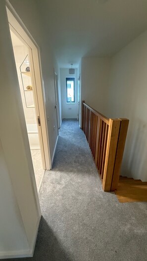 En hall med heltäckningsmatta på golvet, ett träräcke på ena sidan och en dörr på vänster sida.