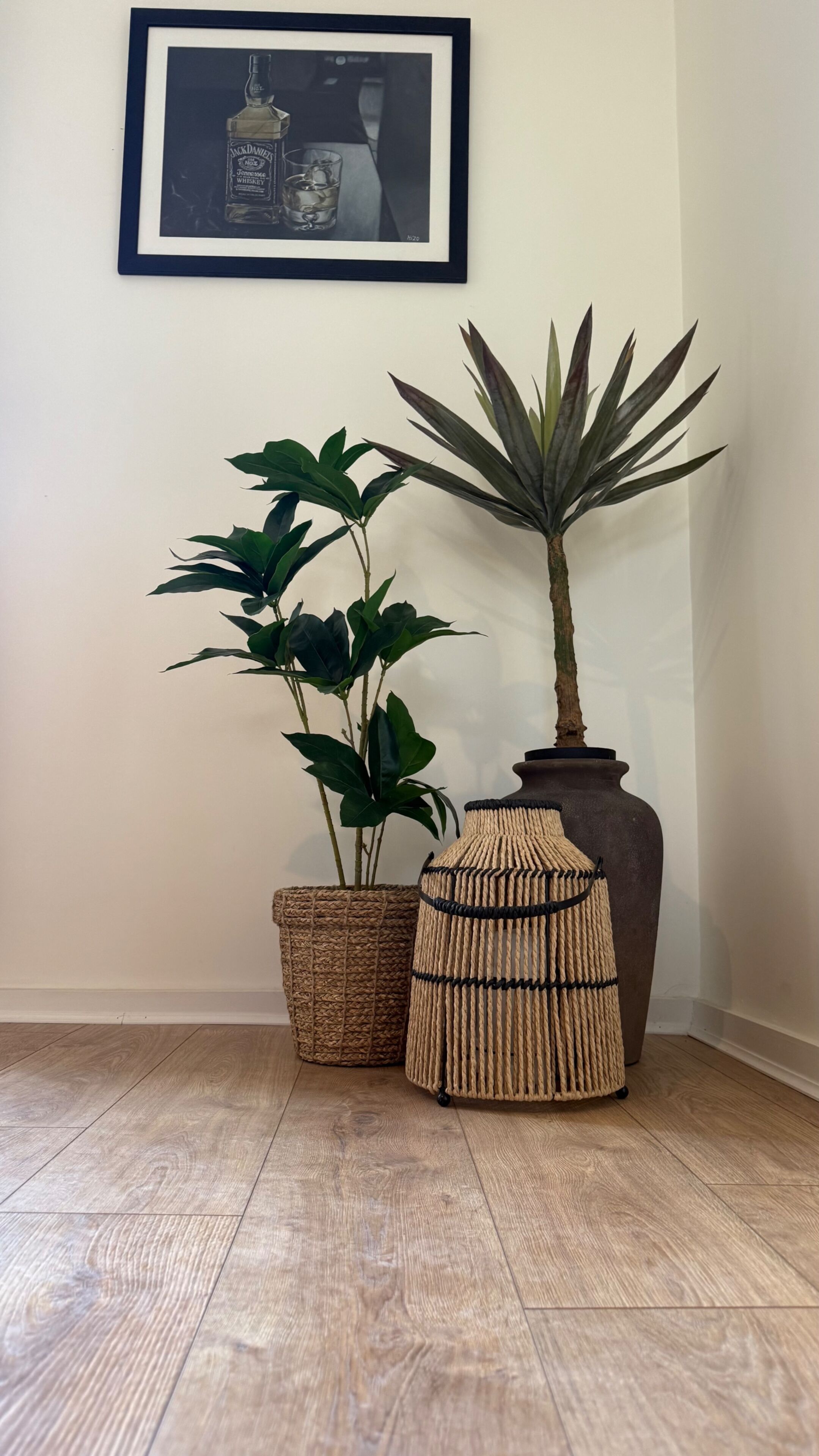 A framed picture, a potted plant, a woven basket, and a large vase on a wooden floor.