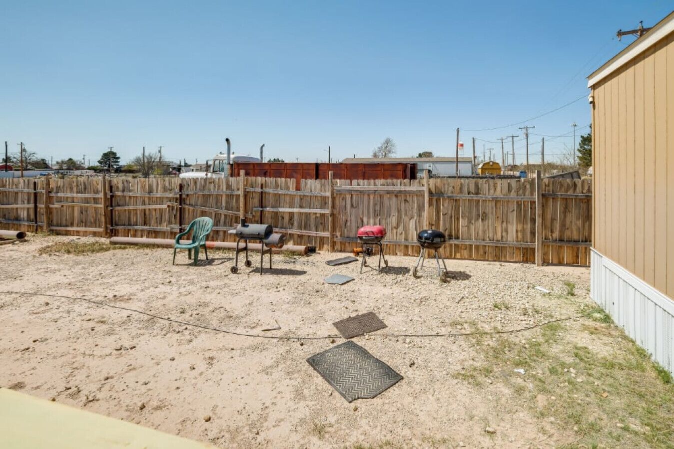 Une cour arrière clôturée avec un barbecue, une chaise et un bâtiment.