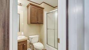 Une salle de bain comprenant des toilettes, un lavabo, un meuble de rangement et une porte de douche.