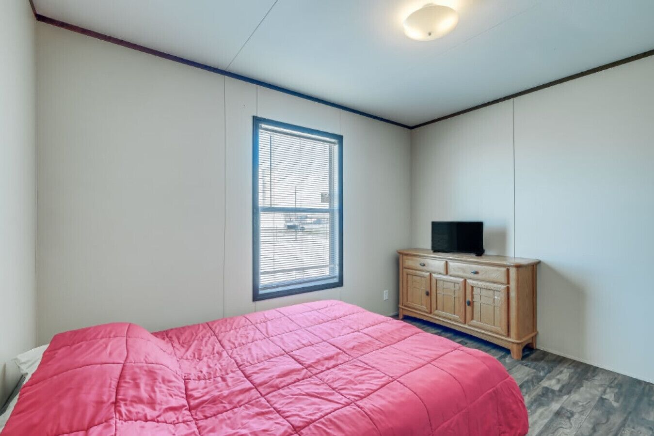 Un dormitorio con una cama, una ventana con persianas, un aparador de madera y un televisor encima.