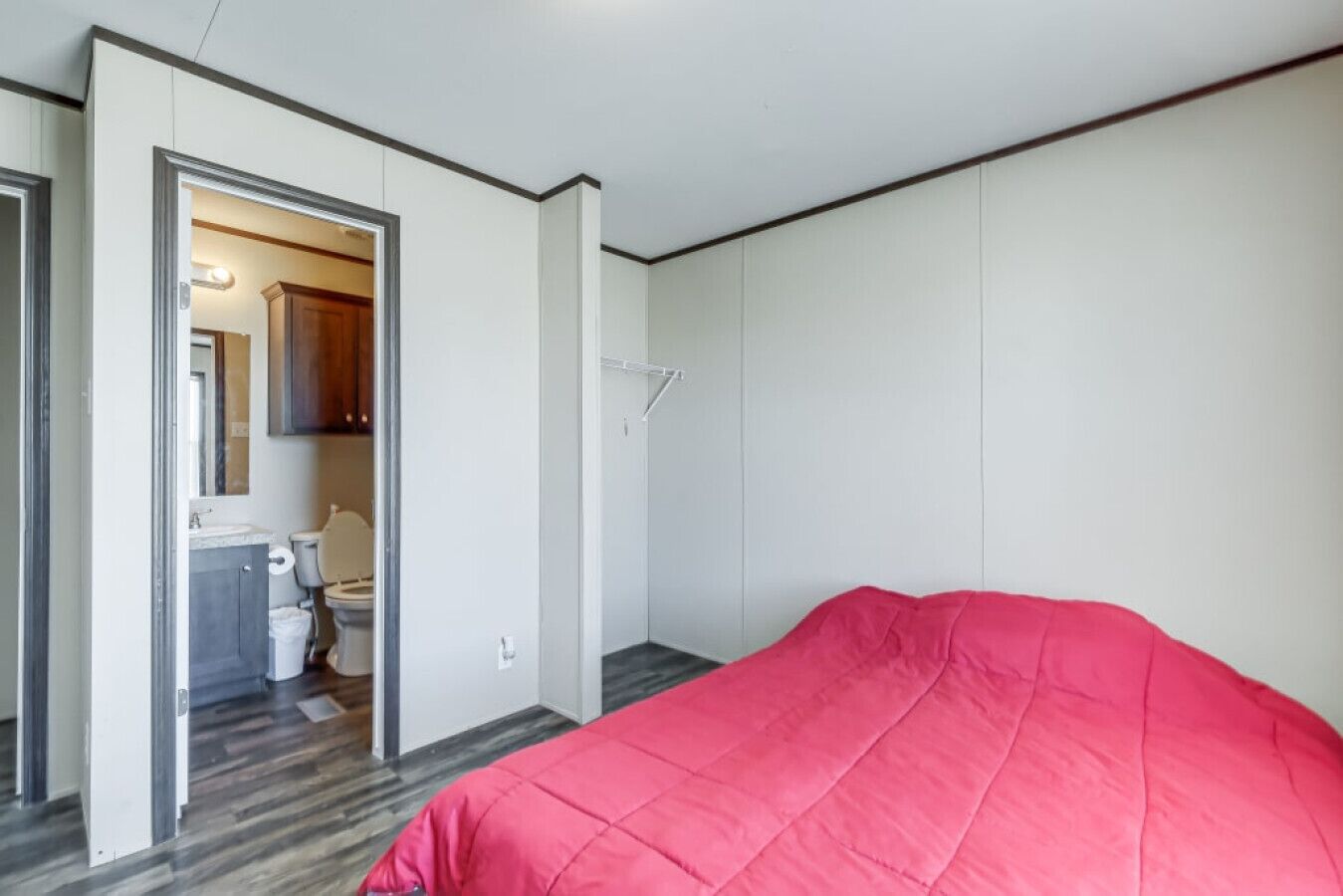 A bedroom with a bed, a door leading to a bathroom, and a visible toilet.