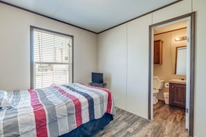 Een slaapkamer met een bed, een raam met zonwering, een televisie en een badkamer die door een open deur zichtbaar is.