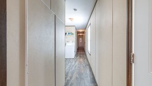 Un couloir étroit, avec une machine à laver au fond, qui mène à une pièce dont la porte se trouve sur la droite.