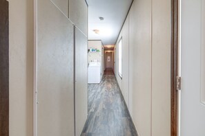 Un pasillo estrecho con una lavadora a lo lejos, que conduce a una habitación con una puerta a la derecha.