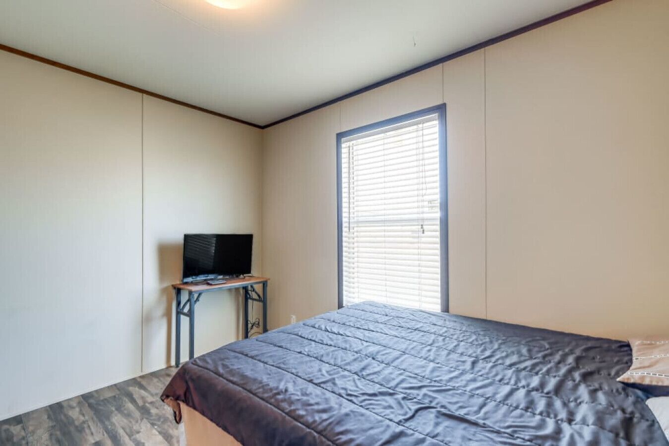 Une chambre à coucher avec un lit, un téléviseur posé sur une petite table et une fenêtre avec des stores.