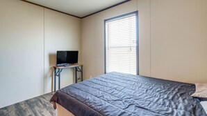 Une chambre à coucher avec un lit, un téléviseur posé sur une petite table et une fenêtre avec des stores.