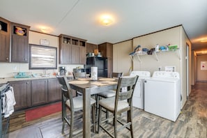 Een compacte keuken met houten kastjes, een eettafel met stoelen, een koelkast en een wasmachine.