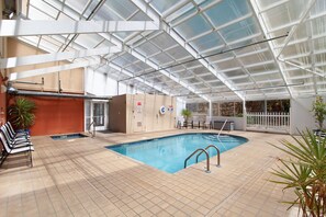 Ein Innenpool mit Glasdecke, gefliestem Boden und einigen Stühlen und Pflanzen.