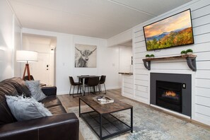 Ein Wohnzimmer mit Kamin, Wandfernseher, Essbereich und einer Couch mit Lampe.
