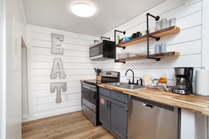 Eine moderne Küche mit weißen Wandverkleidungen, einer Holz Arbeitsplatte, Edelstahlgeräten und einer Küchenutensilien-Regal.