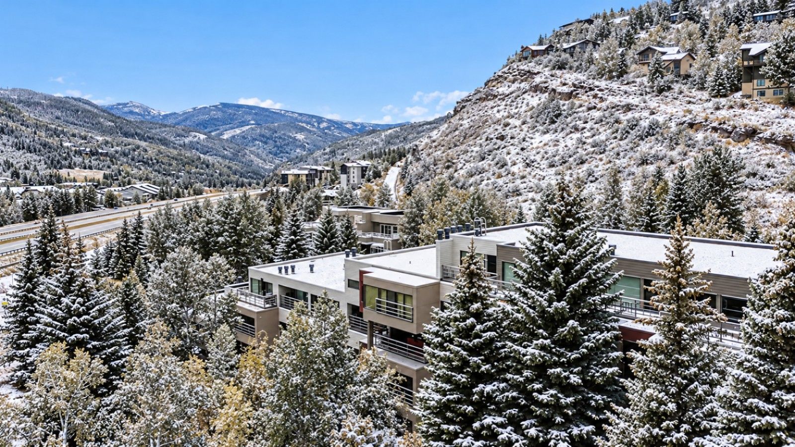 A resort with modern buildings surrounded by snow-covered trees and mountains.