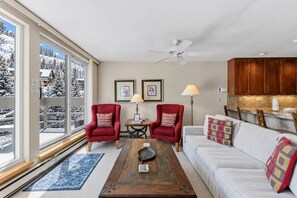 A living room with a large window, two armchairs, a coffee table, a sofa, and a ceiling fan. - Central Condo W/ Resort Amenities I Pool + Hot Tub (Vail)