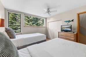 Un dormitorio con dos camas, un televisor sobre un aparador de madera y un ventilador de techo.