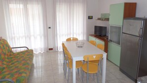 Ein kompakter Wohnbereich mit Esstisch, Stühlen, einer Couch, einem Fernseher und einem Kühlschrank.