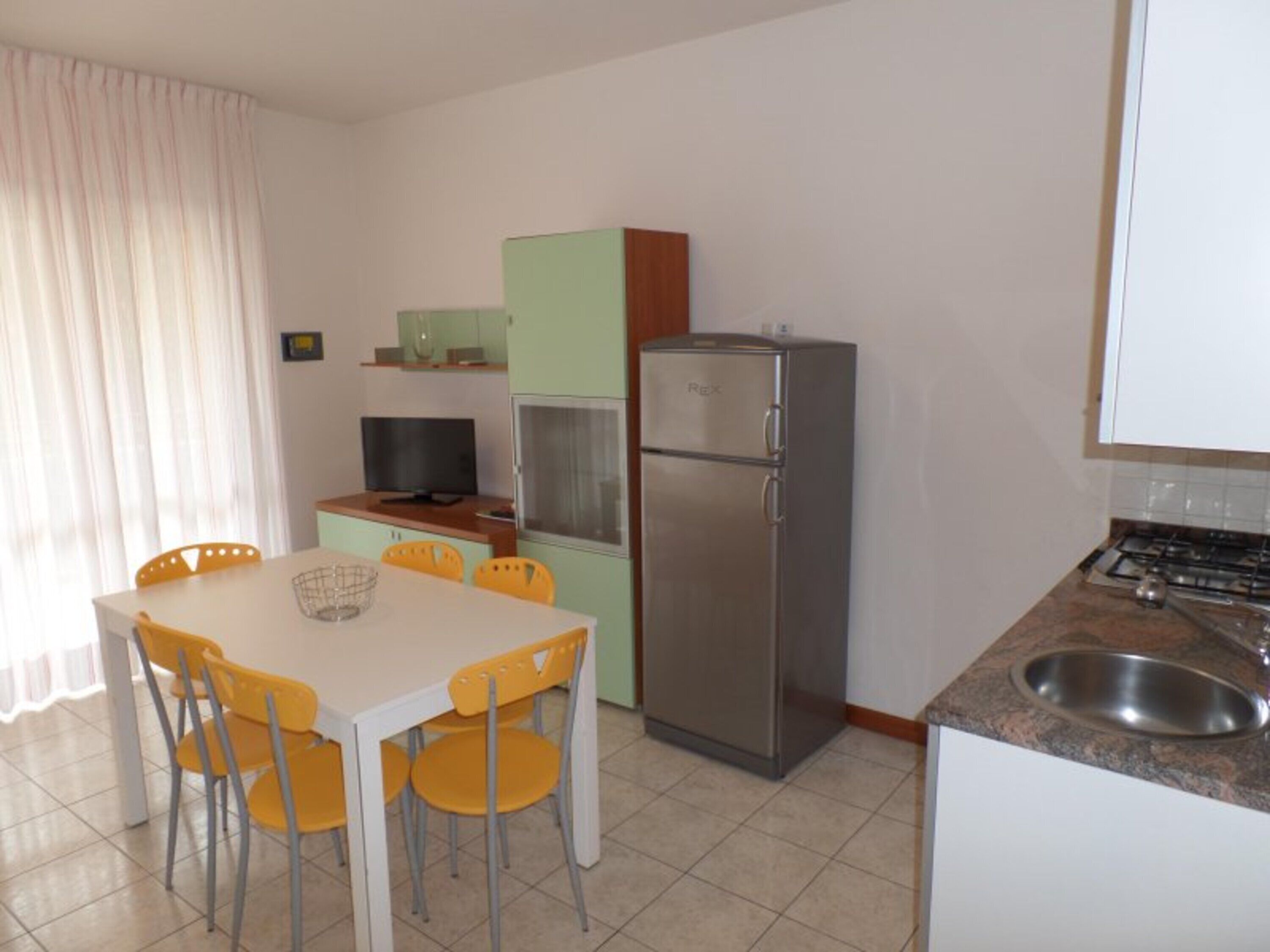 A compact kitchen with a dining table, chairs, a refrigerator, a TV, and a sink.