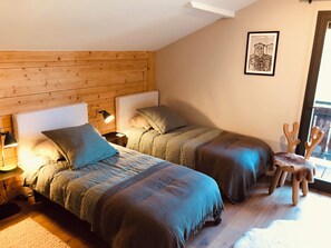 A cozy bedroom with two beds, a wooden headboard, a small table, a chair, and a framed picture on the wall. - PRAZ SUR ARLY Chalet, 5 minutes from MEGEVE—Come experience it for yourself (PRAZ SUR ARLY,)