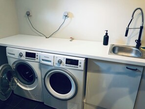 Ett kompakt tvättrum med två tvättmaskiner som har frontmatning, en diskho i rostfritt stål och en blandare.