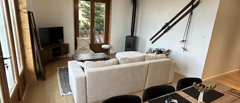 Un salon moderne comprenant un ensemble de canapés, un téléviseur, une cheminée et un coin repas avec une table et des chaises en bois.