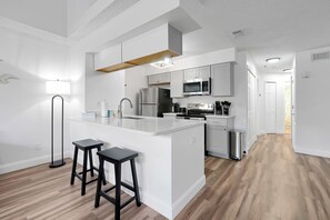 Eine moderne Küche mit weißen Schränken, einer zentralen Kochinsel inklusive Sitzgelegenheiten, einer Mikrowelle und einem Kühlschrank.