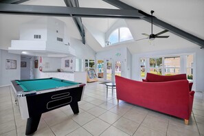 Ein Billardtisch, eine rote Couch und ein Deckenventilator in einem großzügigen Raum mit großen Fenstern und hoher Decke.