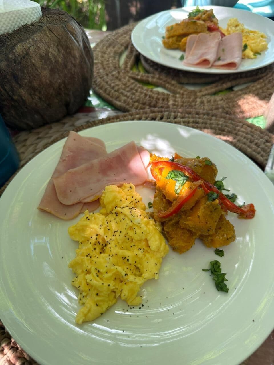 A plate with scrambled eggs, ham, and a vegetable dish, possibly containing bell peppers and onions.