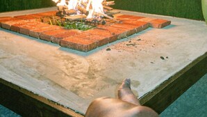 Een vuur brandend op een vierkante bakstenen tafel, met een persoon in de buurt.