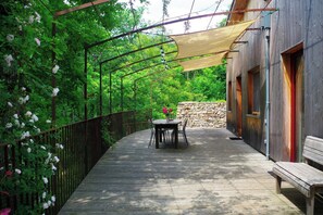 Eine Holzterrasse mit Tisch und Stühlen, eine Steinmauer und ein Gebäude mit Fenstern.