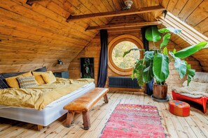 Ein gemütliches Schlafzimmer im Dachgeschoss mit Bett, Bank, Blumentöpfen und einem Rundfenster.