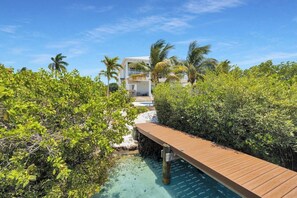 Eine Holzterrasse führt zu einem Gebäude mit einem Pool, umgeben von üppiger Vegetation und klarem, blauem Wasser.