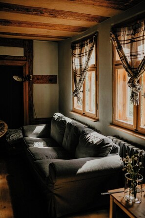 Ein gemütliches Zimmer mit einer Couch, einem Tisch mit einer Vase und einem Fenster mit Vorhängen.