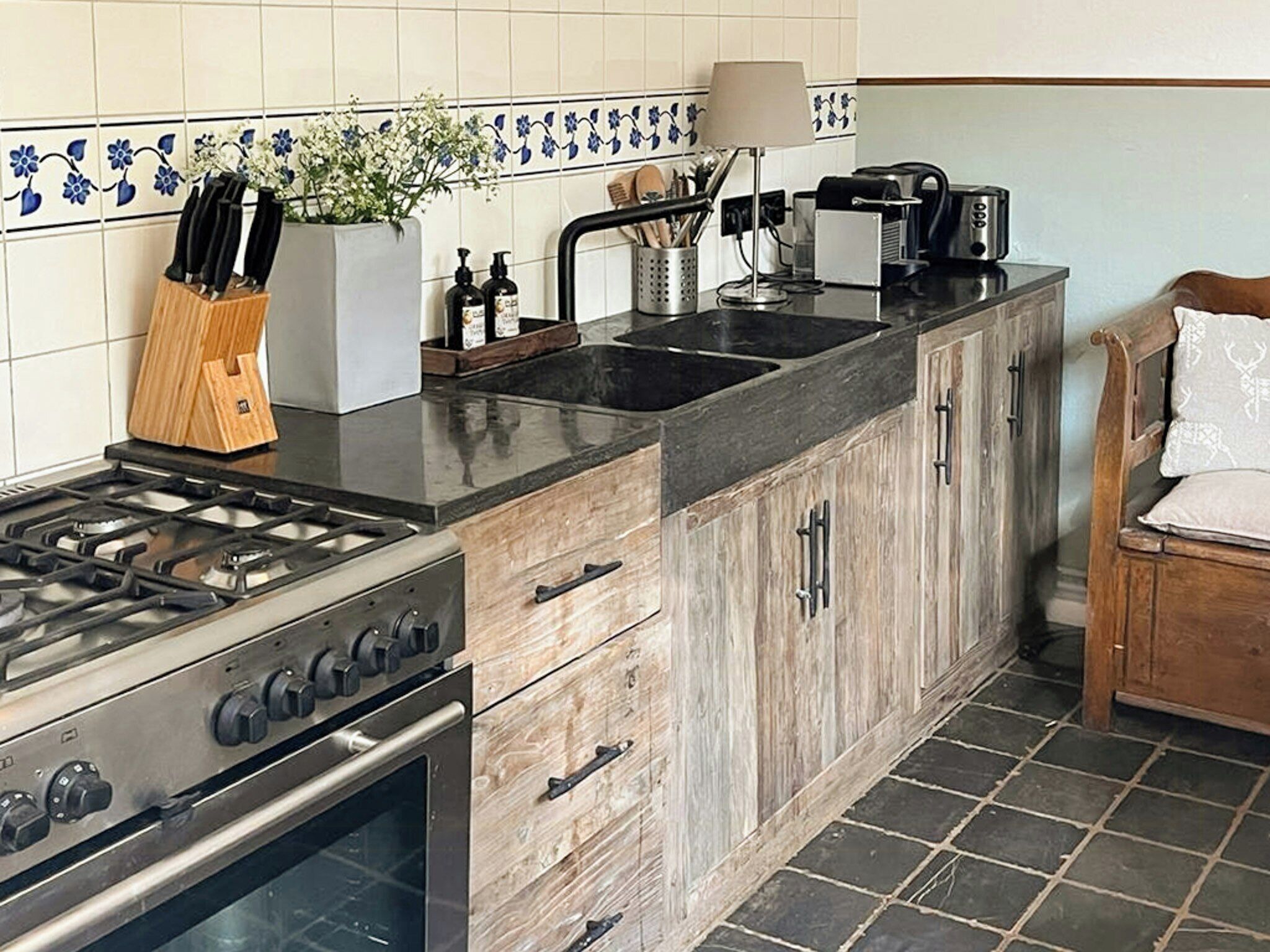 A kitchen with a gas stove, oven, wooden cabinets, a sink, and a coffee maker.