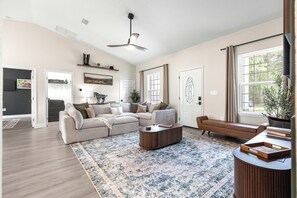 A spacious living room with a large sofa, a coffee table, and a floor lamp. There is a door leading to another room and a window with curtains. - Horse Country Escape 15 Minutes to WEC & Adventure Springs (Lutz)