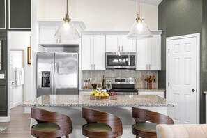 A modern kitchen with white cabinets, stainless steel appliances, and a granite island with bar seating. - Horse Country Escape 15 Minutes to WEC & Adventure Springs (Ocala)