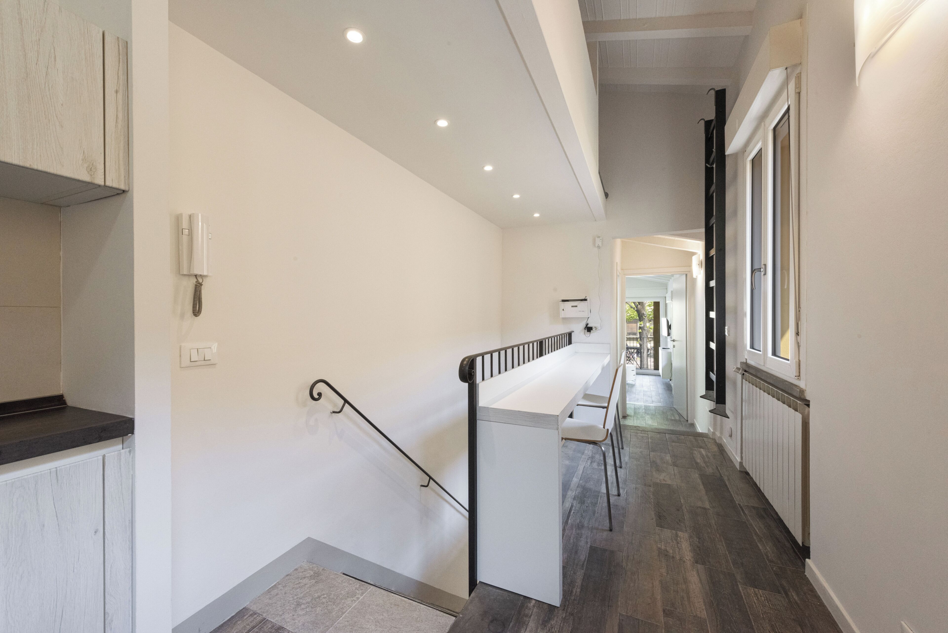 A modern interior with a staircase, a kitchen area, and a hallway leading to a door.