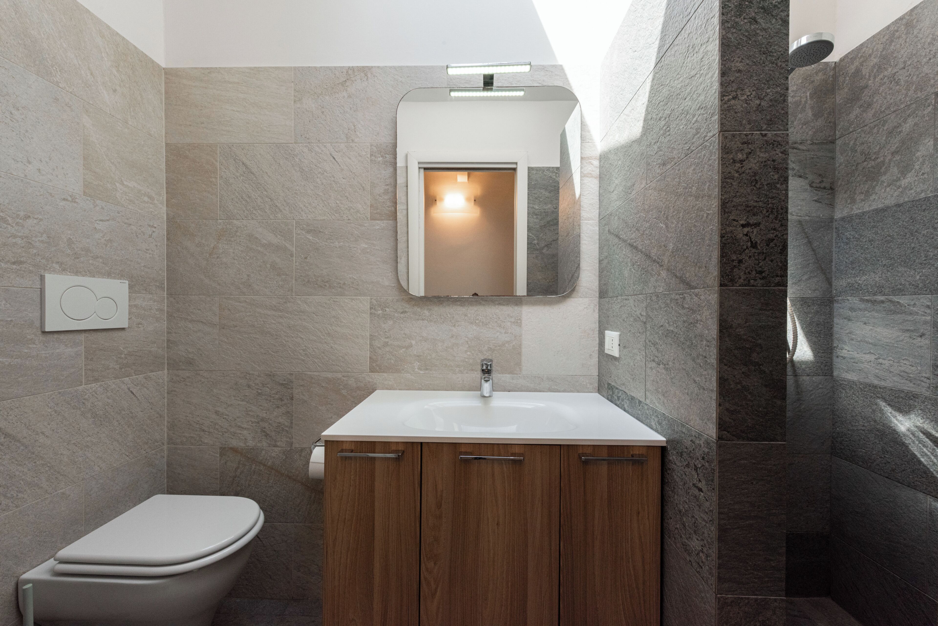 A bathroom with a toilet, wooden cabinets, a white sink, a mirror, and a shower.