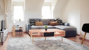 En moderne stue med sofa, sofabord, fjernsyn og et lille sengebord.