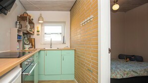 Una cocina compacta con ventana, una cama con colcha estampada y una pared de ladrillo.