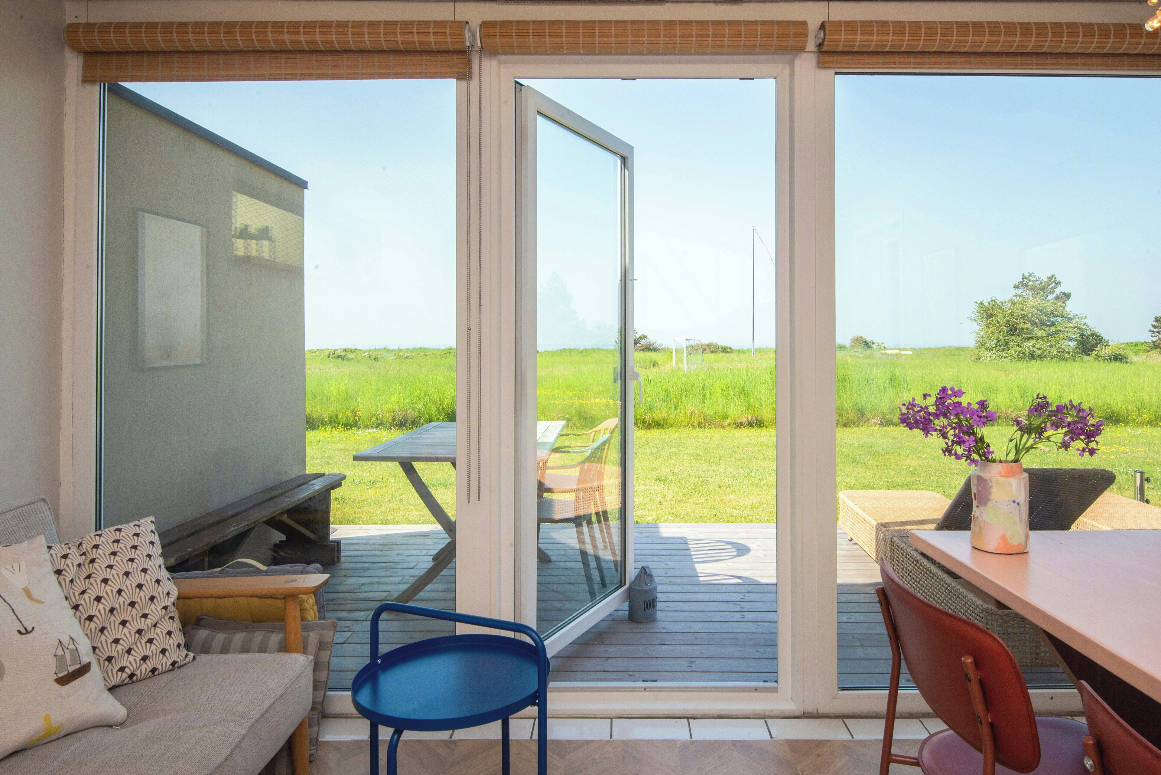 A room with a sliding glass door leading to an outdoor deck, a sofa, a TV, and a table with chairs.