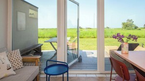 Una habitación con puerta corrediza de vidrio que da a una terraza exterior, un sofá, un televisor y una mesa con sillas.