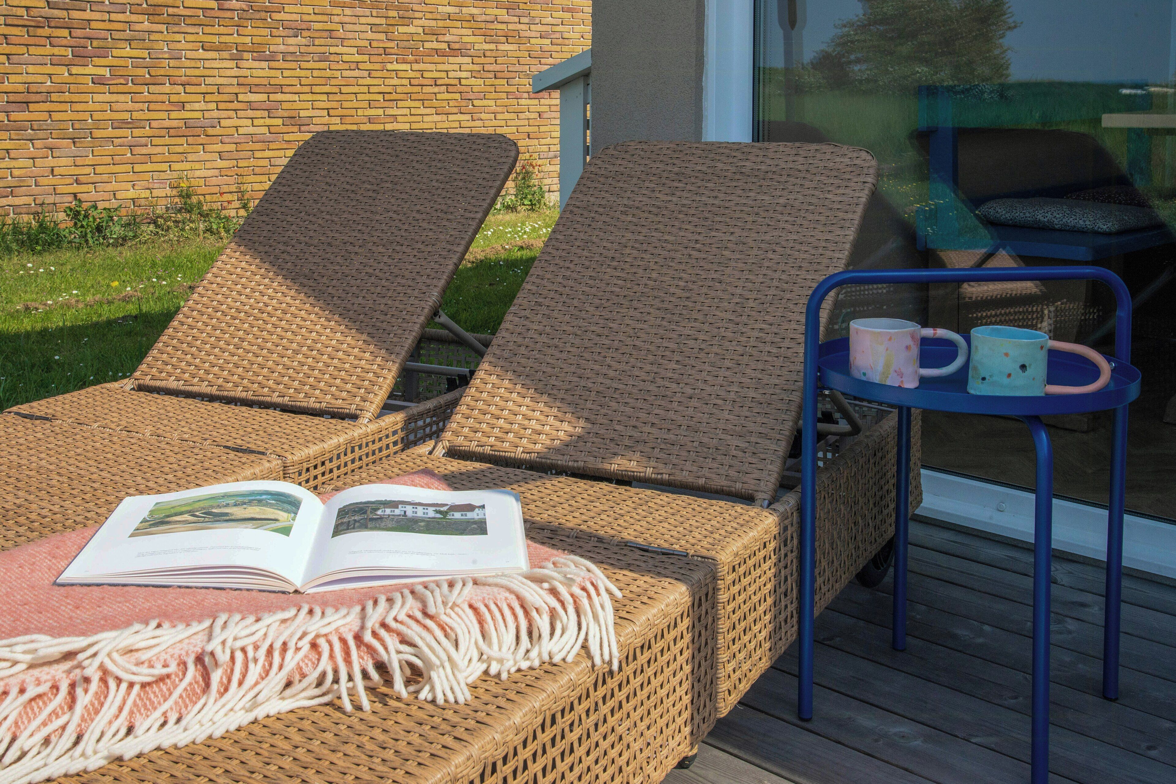 Wicker lounge chairs with a blanket and a tray table with mugs.