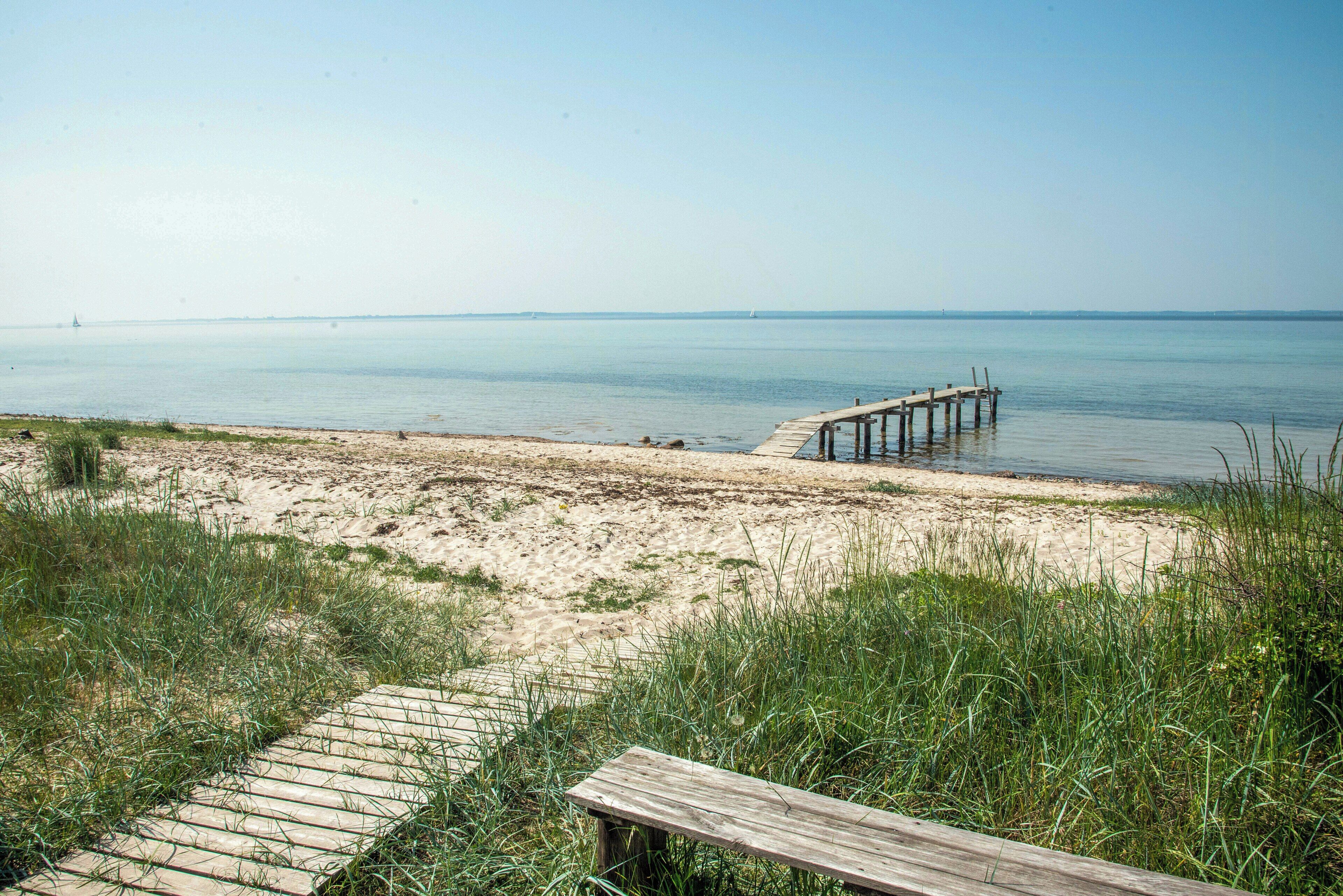 Ein Strand mit einer Holzpromenade, die zu einem Steg in ruhigem Wasser führt.