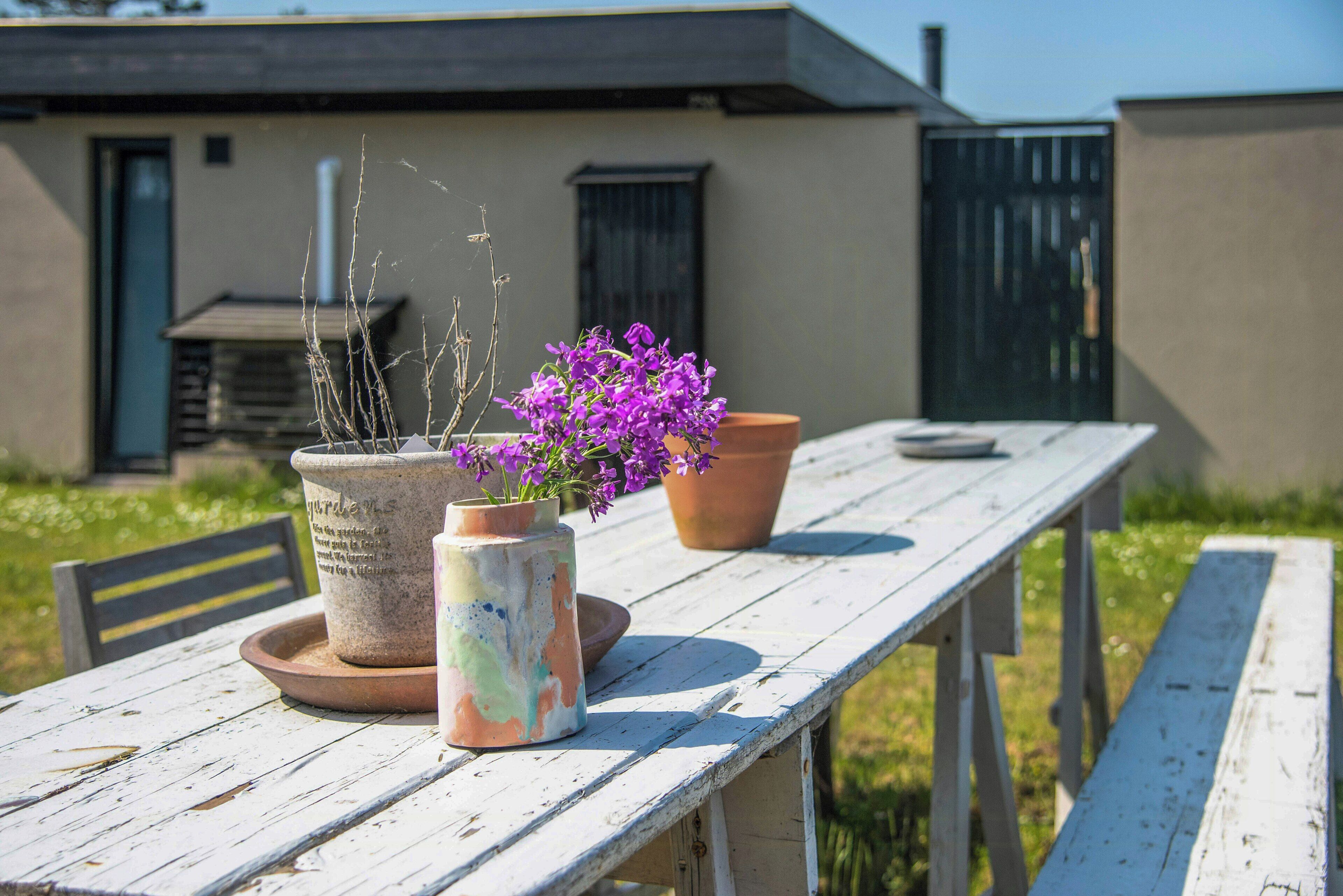 A rustic wooden table with two potted plants and a bench.