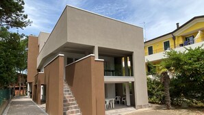 A modern building with a flat roof, a staircase leading to an upper level, and a patio area with outdoor seating. - Modern Stay in a Central Area in Bibione (San Michele al Tagliamento)